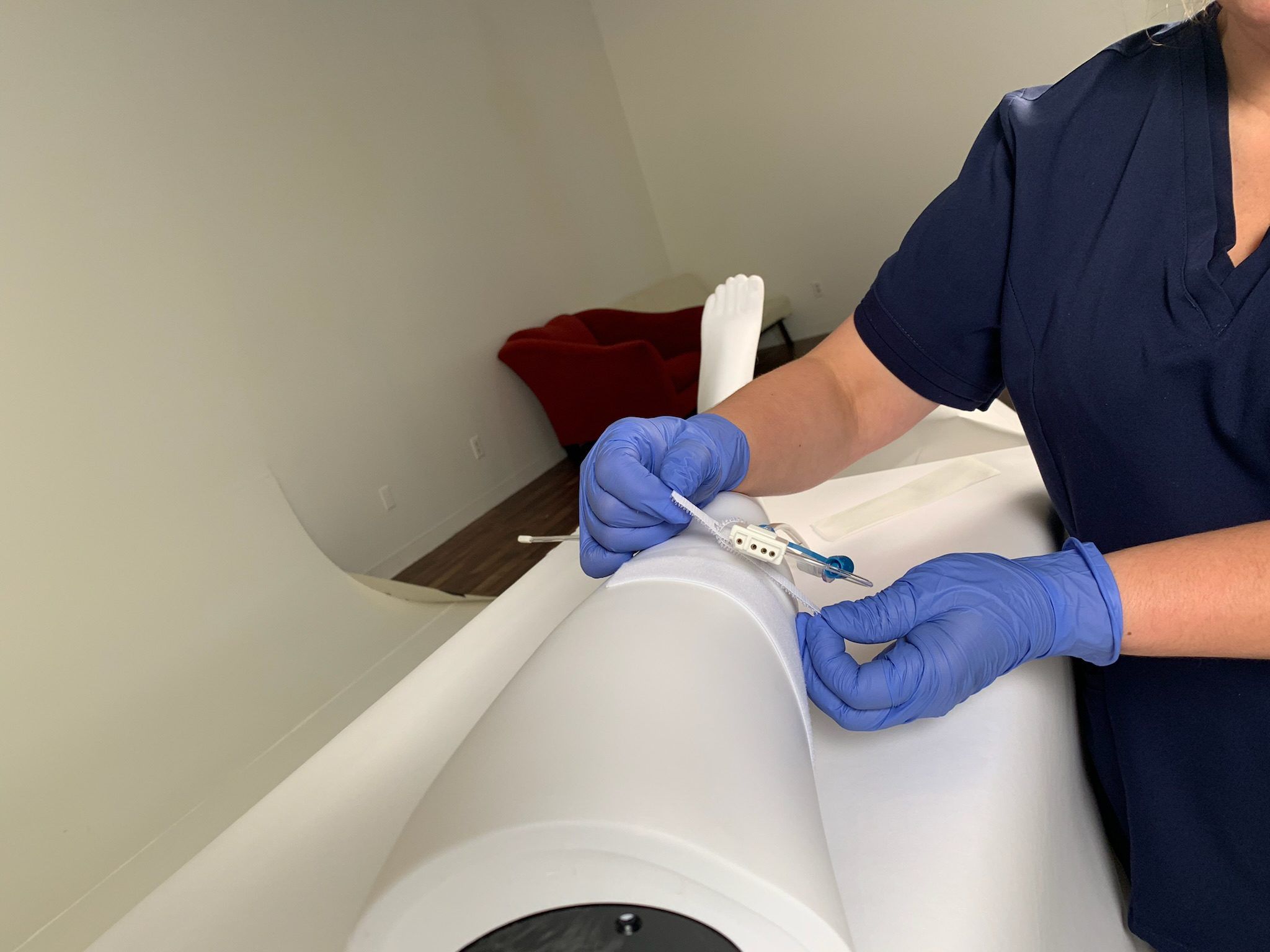 A healthcare professional wearing blue gloves and scrubs practices a medical procedure with a catheter on the leg of a high-fidelity training mannequin in a simulation lab.